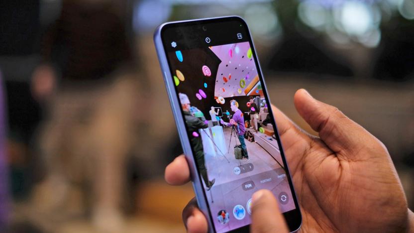 A cropped image shows two hands holding up a Samsung Galaxy A53 smartphone with a colorful event being shown on the phone's screen as the camera is activated.