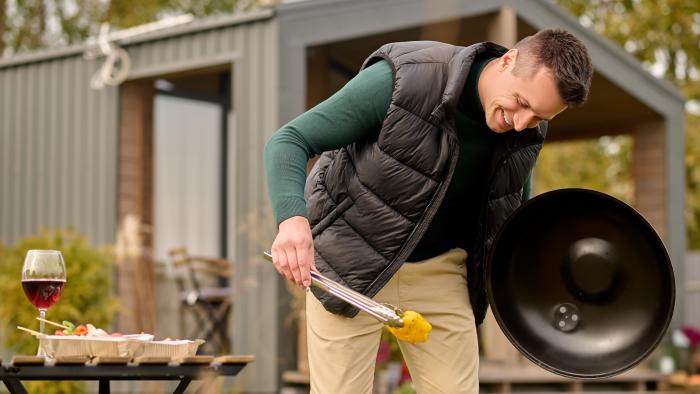 Smiling man leaning over the open brazier and gripping the slice of bell pepper with barbecue tongs