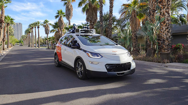 A GM Cruise vehicle driving down a palm tree-lined street.