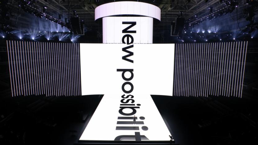 Stage with huge ultrawide screen on the back, and a perpendicular screen stretching above and below it onto the runway. "New possibilities" on the screen.