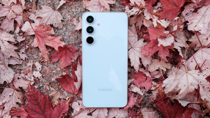 A blue Galaxy S24 FE sits on a pile of red maple tree leaves with the concrete sidewalk below. 